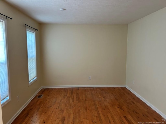 spare room with a wealth of natural light, baseboards, visible vents, and wood finished floors