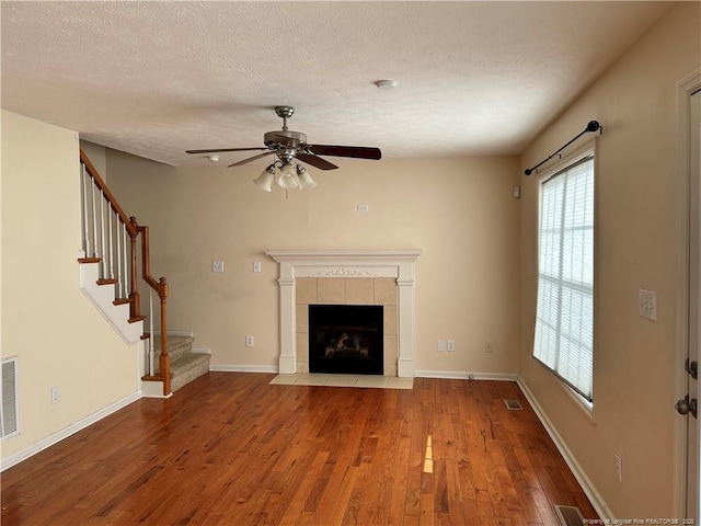 unfurnished living room with a textured ceiling, ceiling fan, stairs, wood finished floors, and a fireplace