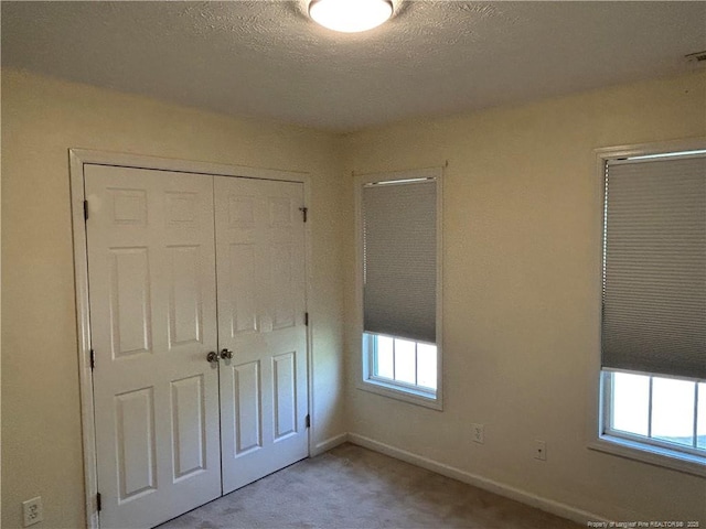 unfurnished bedroom with baseboards, a textured ceiling, a closet, and carpet floors