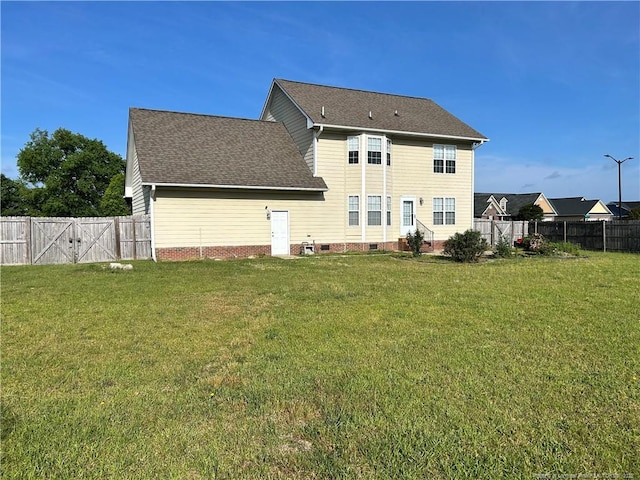 rear view of house featuring a lawn, a shingled roof, and a fenced backyard