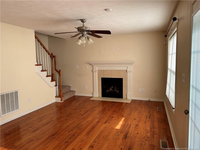 1901 Ellie Ave, Fayetteville, NC 28314 - unfurnished living room featuring wood finished floors, a ceiling fan, a tiled fireplace, stairway, and a textured ceiling