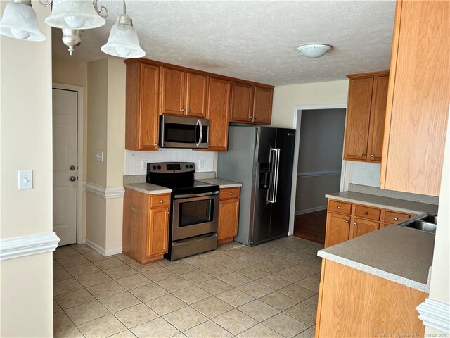 1901 Ellie Ave, Fayetteville, NC 28314 - kitchen with appliances with stainless steel finishes, light tile patterned floors, decorative backsplash, brown cabinetry, and a textured ceiling