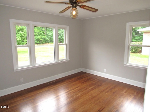 empty room with baseboards, a ceiling fan, visible vents, and dark wood finished floors