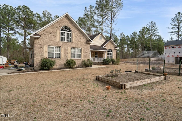 view of front of home with a porch, fence, brick siding, a front yard, and a garden