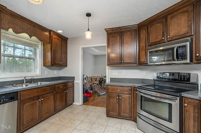 kitchen with pendant lighting, light tile patterned floors, a sink, dark countertops, and stainless steel appliances