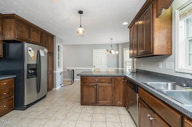 kitchen with a textured ceiling, a sink, a peninsula, dark countertops, and appliances with stainless steel finishes