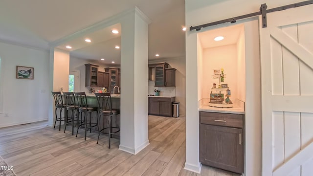 2912 Epps Clark Rd, Siler City, NC 27344 - kitchen with a barn door, a breakfast bar area, light wood finished floors, recessed lighting, and glass insert cabinets
