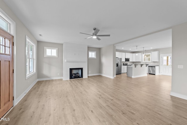 unfurnished living room with baseboards, a fireplace, light wood-type flooring, and plenty of natural light