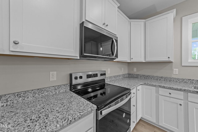 kitchen with white cabinets, appliances with stainless steel finishes, light wood finished floors, and light stone countertops