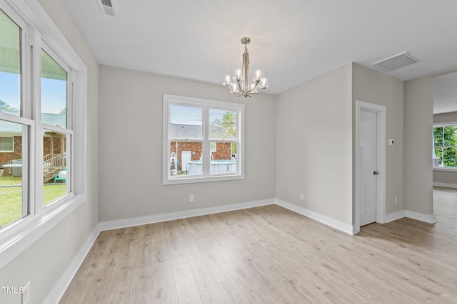 empty room featuring a chandelier, baseboards, visible vents, and light wood-style floors