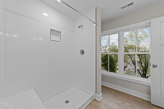 full bath featuring wood finished floors, visible vents, baseboards, and tiled shower