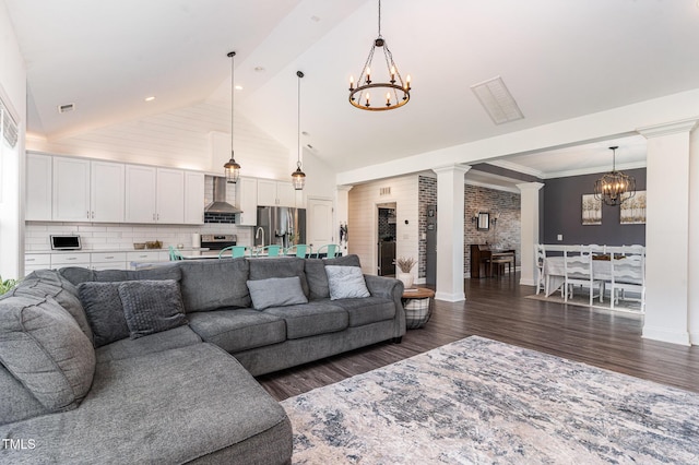 living area featuring a chandelier, decorative columns, dark wood finished floors, lofted ceiling, and baseboards