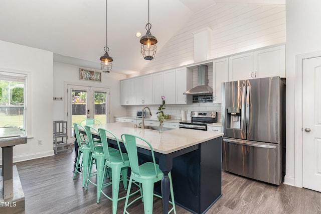 kitchen with stainless steel appliances, wall chimney range hood, a sink, dark wood-style floors, and tasteful backsplash