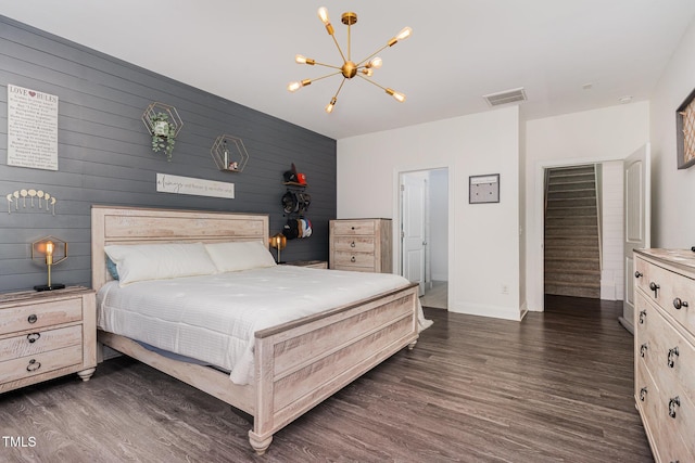bedroom with a chandelier, dark wood-style flooring, baseboards, wooden walls, and an accent wall