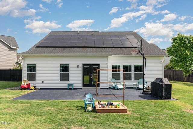 rear view of property with a patio area, roof mounted solar panels, and a shingled roof