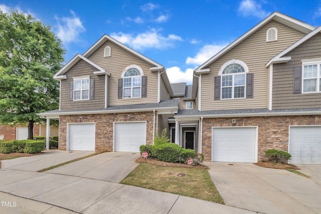 townhome / multi-family property with driveway, a garage, and stone siding