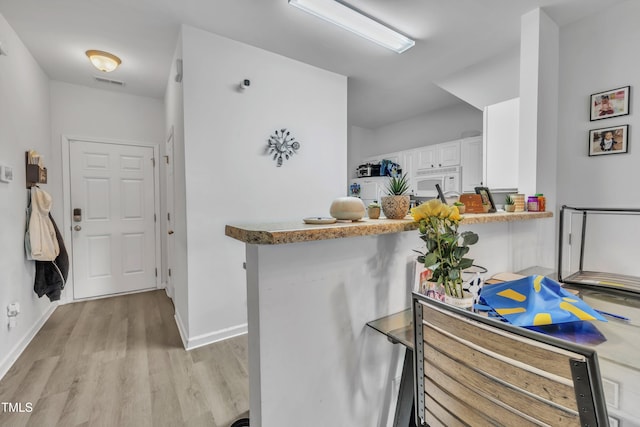 kitchen with light wood finished floors, white cabinetry, baseboards, white microwave, and a peninsula