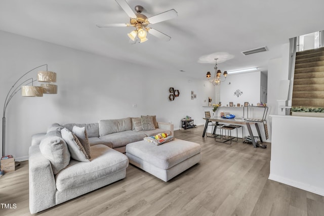 living area featuring stairs, wood finished floors, a ceiling fan, and a chandelier