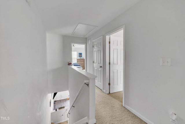 corridor with attic access, an upstairs landing, light carpet, and baseboards