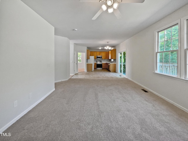 unfurnished living room with baseboards, a healthy amount of sunlight, visible vents, ceiling fan with notable chandelier, and light carpet
