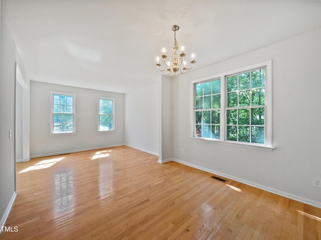 spare room with baseboards, a notable chandelier, visible vents, and light wood-type flooring