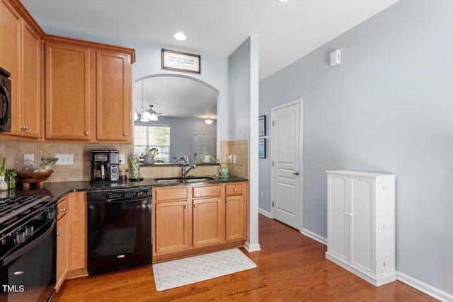 kitchen with black appliances, a sink, decorative backsplash, light wood-type flooring, and arched walkways