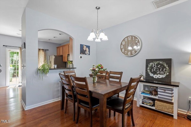 dining space featuring arched walkways, wood finished floors, a chandelier, and baseboards