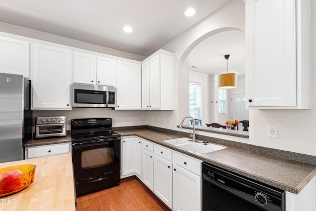 kitchen with black appliances, a sink, arched walkways, white cabinetry, and recessed lighting