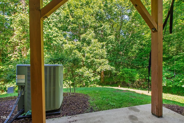 view of green lawn featuring central AC unit, a patio area, and a view of trees