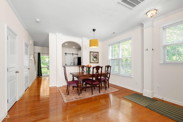 dining area featuring decorative columns, wood finished floors, crown molding, baseboards, and a barn door