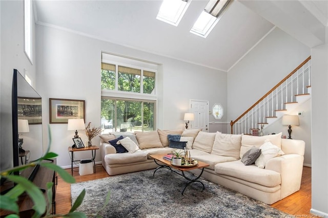 living room featuring stairs, crown molding, high vaulted ceiling, wood finished floors, and a skylight