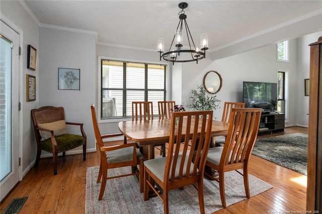 dining space with baseboards, visible vents, crown molding, light wood-style flooring, and a notable chandelier