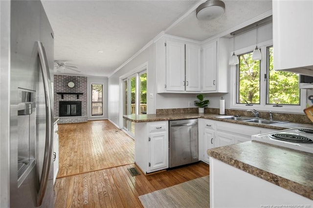 kitchen featuring a sink, dark wood-type flooring, a brick fireplace, dark countertops, and appliances with stainless steel finishes