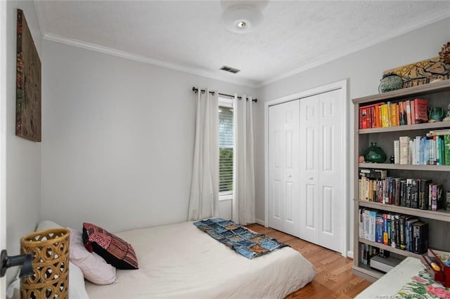 bedroom with crown molding, a closet, visible vents, and wood finished floors