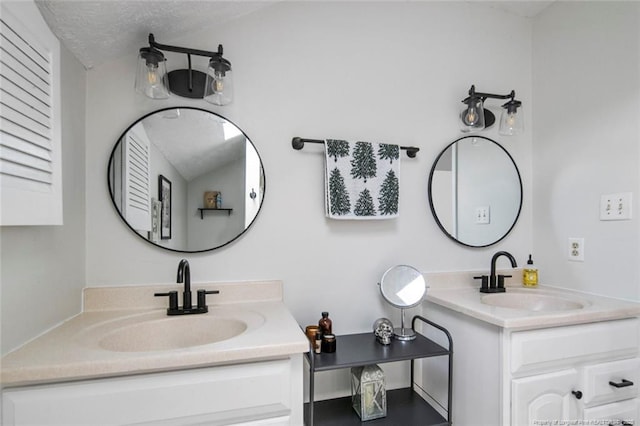full bath featuring a sink, a textured ceiling, and two vanities