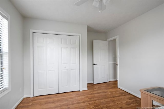 unfurnished bedroom featuring baseboards, multiple windows, a closet, and wood finished floors
