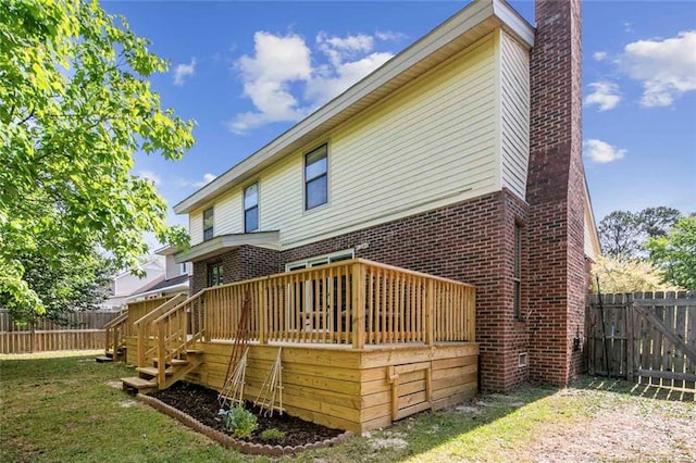 back of house with brick siding, a chimney, a wooden deck, and a fenced backyard