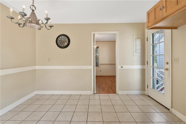 unfurnished dining area featuring crown molding, light tile patterned flooring, a notable chandelier, and baseboards