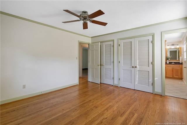 unfurnished bedroom featuring connected bathroom, multiple closets, crown molding, baseboards, and light wood-style floors
