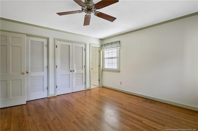 unfurnished bedroom with baseboards, ornamental molding, visible vents, wood finished floors, and multiple closets