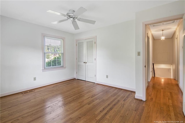 unfurnished bedroom with wood finished floors, a ceiling fan, a closet, visible vents, and baseboards