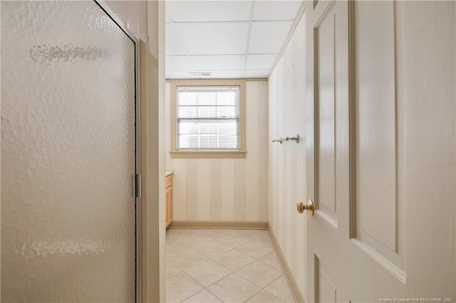 corridor with a paneled ceiling, baseboards, and light tile patterned floors