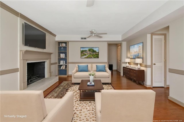living room featuring a fireplace with raised hearth, visible vents, wood finished floors, and a ceiling fan