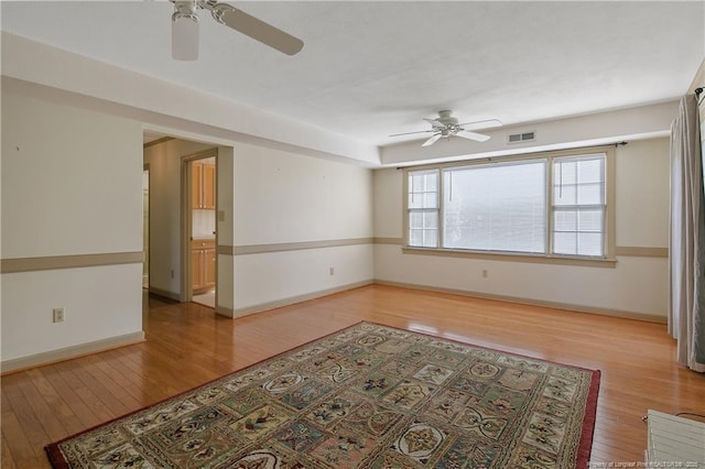 empty room featuring light wood-style floors, visible vents, baseboards, and a ceiling fan
