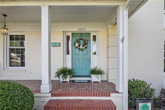 entrance to property featuring a porch and brick siding
