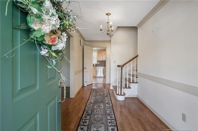 foyer entrance featuring baseboards, ornamental molding, an inviting chandelier, stairs, and wood finished floors