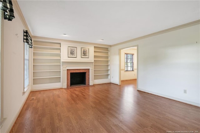 unfurnished living room featuring wood finished floors, a fireplace, crown molding, baseboards, and built in shelves