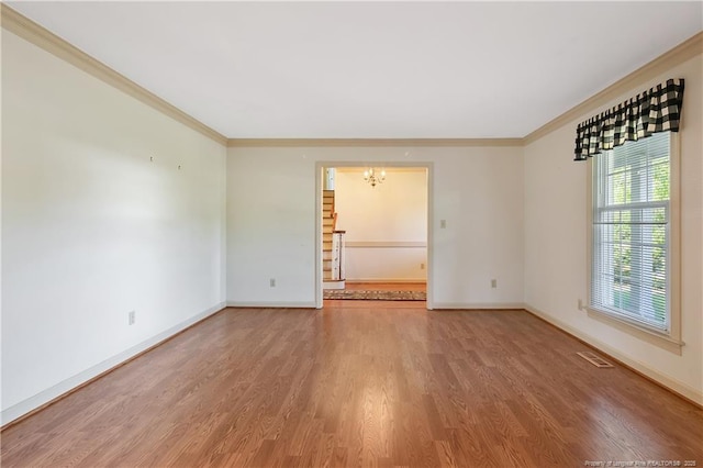 empty room with baseboards, ornamental molding, an inviting chandelier, and wood finished floors