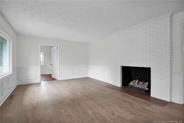 unfurnished living room with a textured ceiling, a brick fireplace, a decorative wall, a wainscoted wall, and wood finished floors