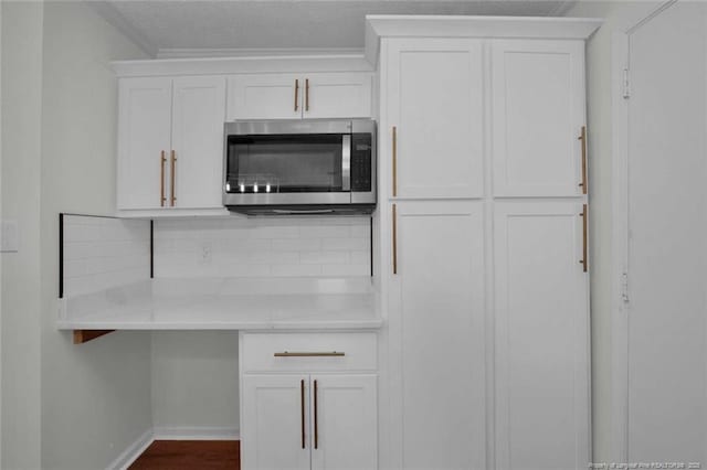 interior space featuring baseboards, stainless steel microwave, white cabinetry, backsplash, and light countertops